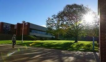 Sun shining on campus with a student walking by a building